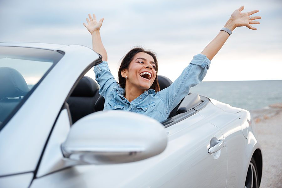 Insurance Quote - Portrait of an Excited Young Woman Sitting in a Convertible Car While on a Road Trip By the Coast