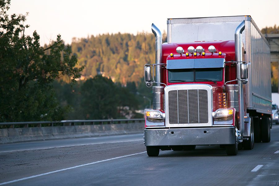 Specialized Business Insurance - Closeup View of a Red Tractor Trailer Truck Driving on the Highway with Views of the Mountains in the Background